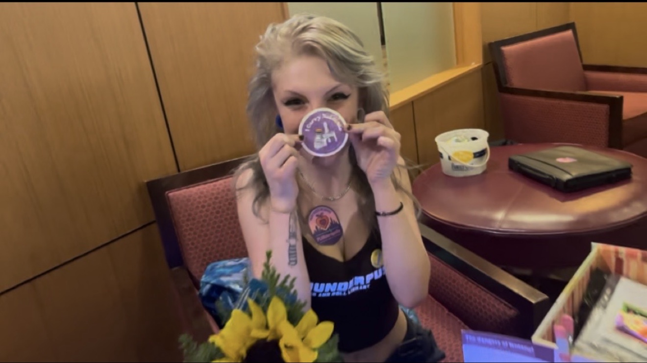 PLURderapolis volunteer holding up a sticker at the harm reduction booth