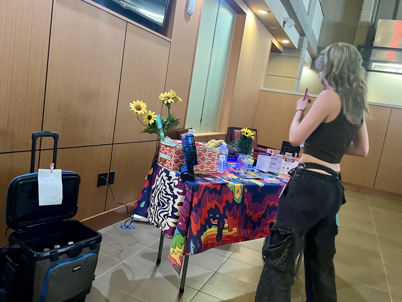 PLURderapolis harm reduction booth table with a colorful cloth, sunflowers, and free supplies at a Twin Cities event